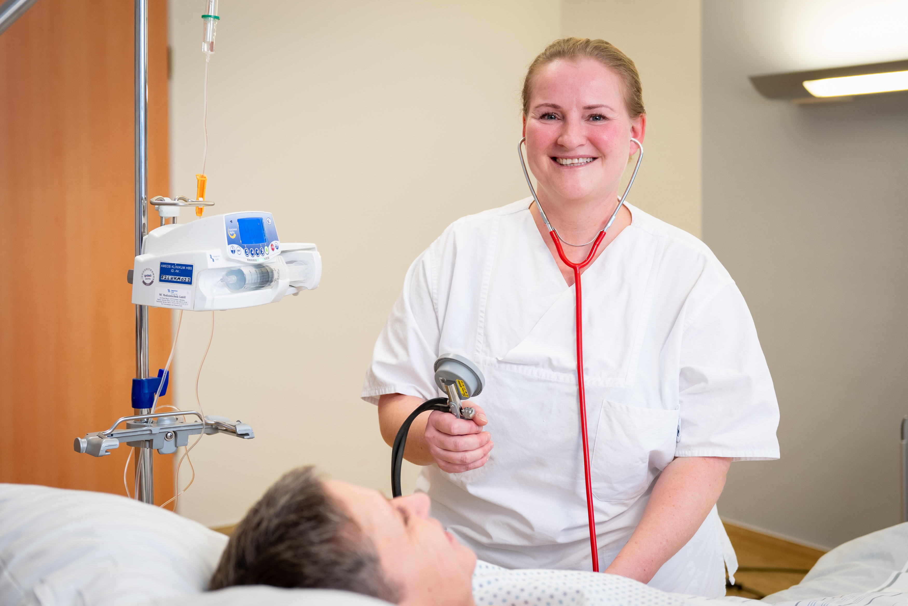 Eine Pflegefachkraft steht am Bett einer Patientin und misst den Blutdruck.