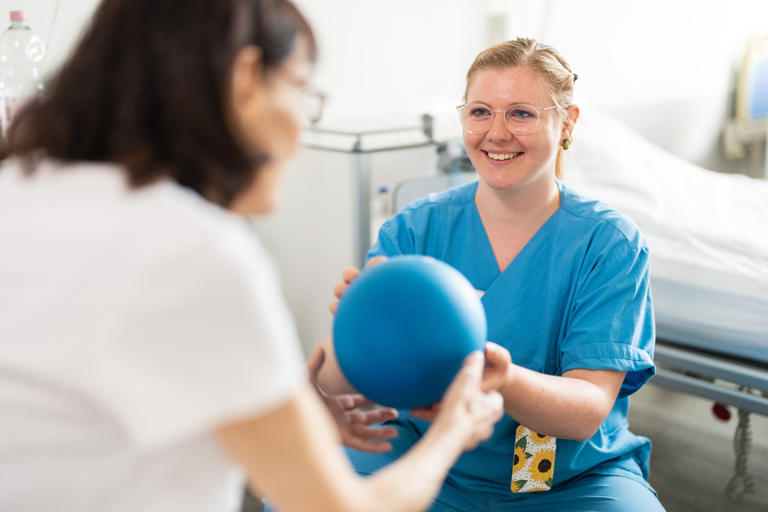 Patientin nimmt Ball von Physiotherapeutin entgegen